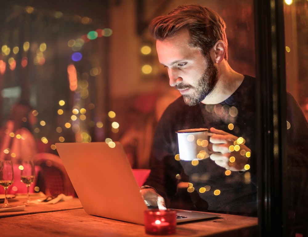 Man looking at his laptop and holding a mug.